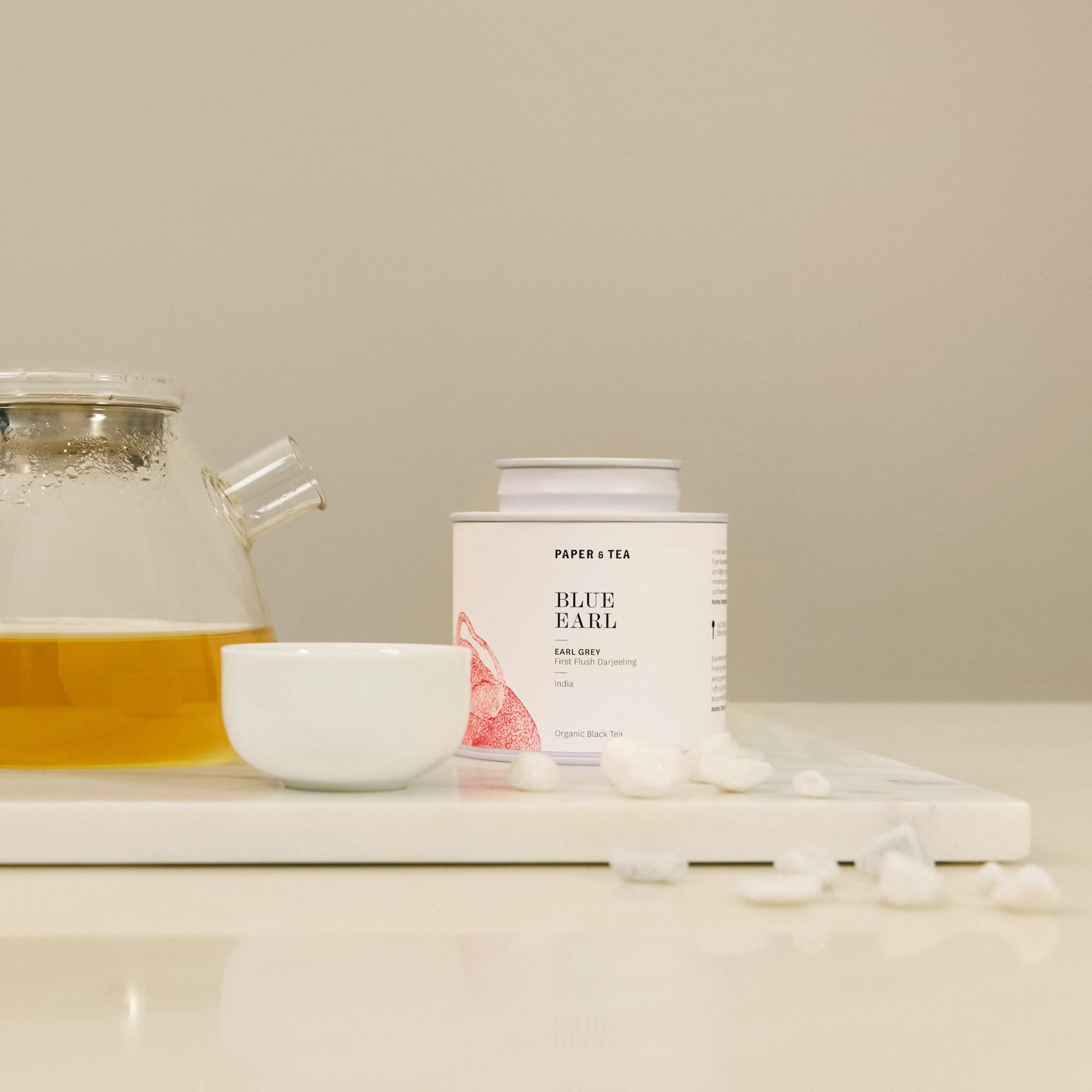 Weiße zylindrische Dose mit P & T Blue Earl Grey Bio-Darjeeling, Glasteekanne mit Tee und weiße Teetasse