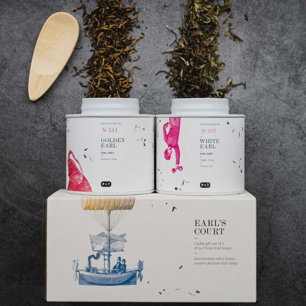 Zwei weiße Teedosen mit GOLDEN EARL und WHITE EARL Tee, im EARL'S COURT Geschenkset mit Holzlöffel und Teeblättern.