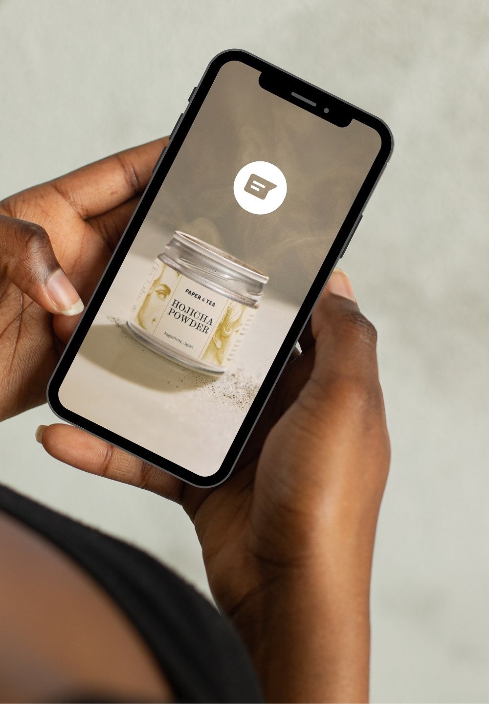 Hände mit dunkler Hautfarbe halten Smartphone mit Bild von Paper & Tea Hojicha Pulver aus Kagoshima, Japan