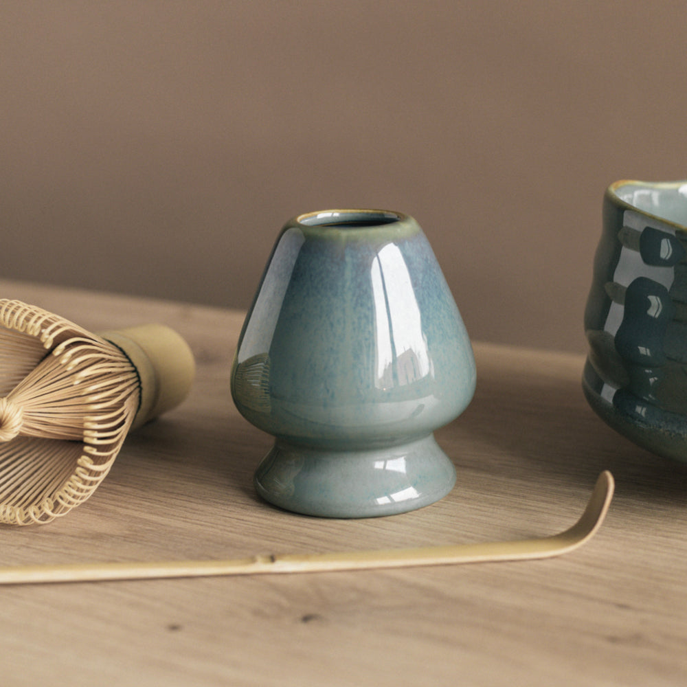 Glänzender blauer-grüner Keramikhalter für Matcha-Besen, Bambusbesen und Keramik-Teeschale auf Holzplatte.