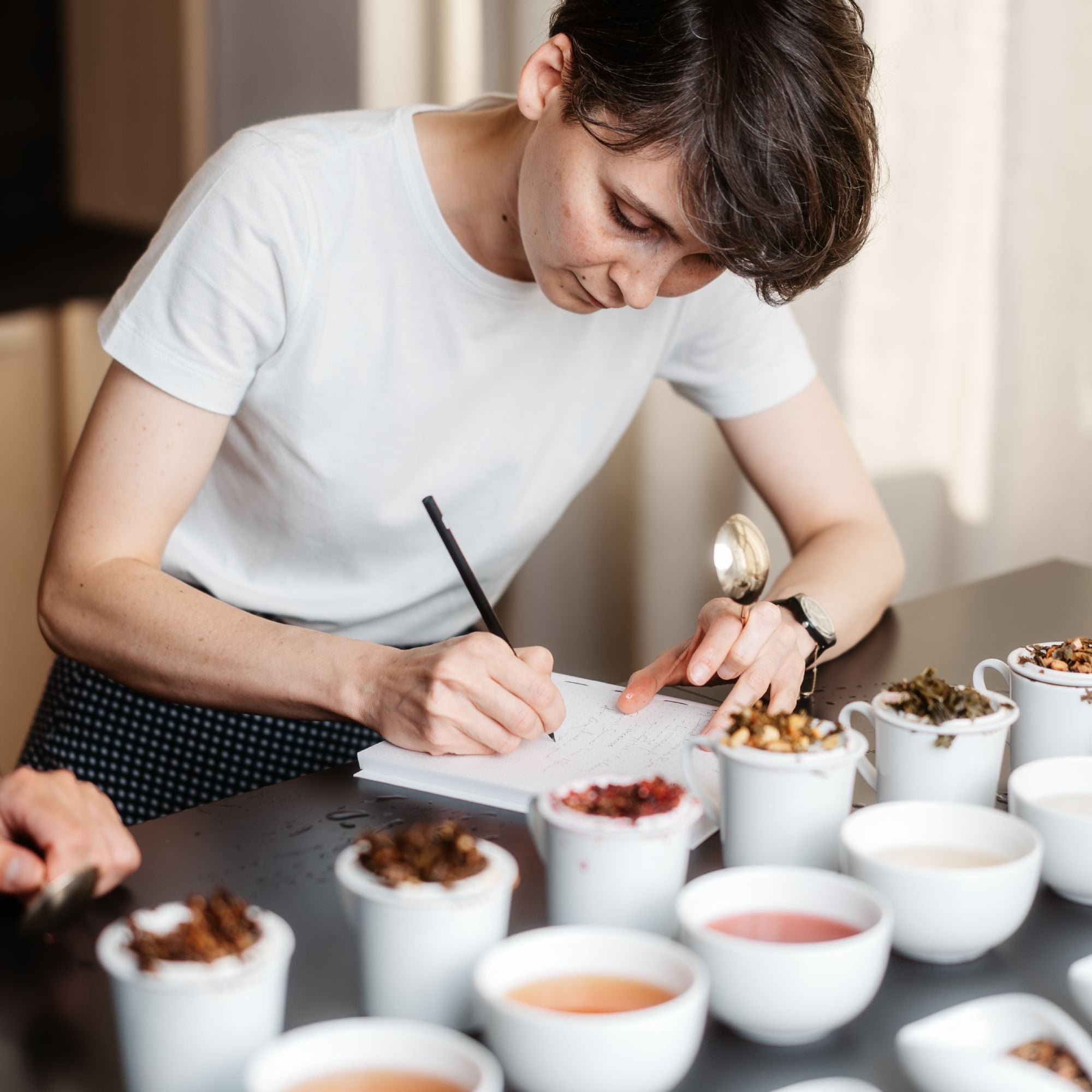 Junge Person in weißem T-Shirt bei einer Teeverkostung mit Keramiktassen voller diverser Teesorten
