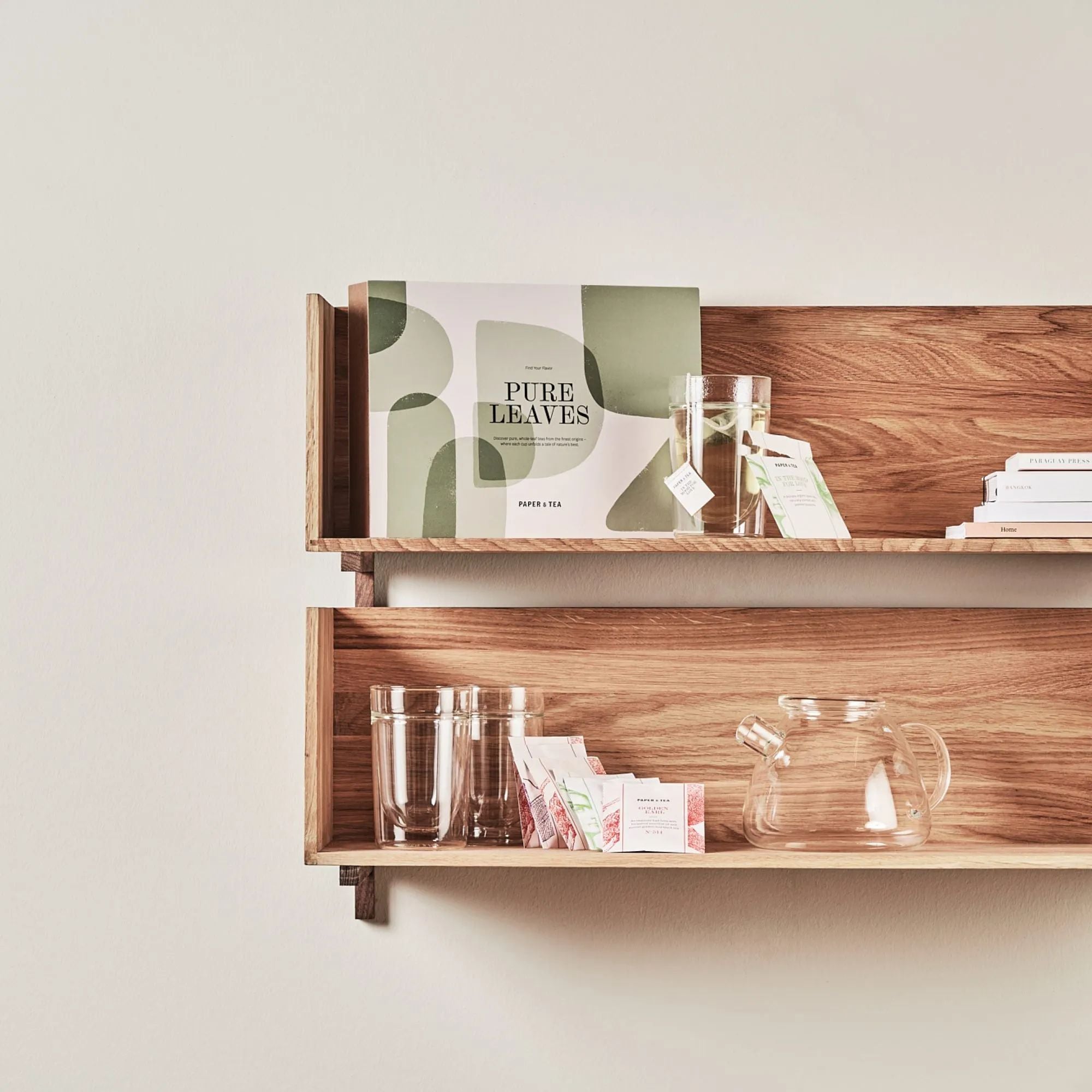 Holzregale mit PURE LEAVES Teepaket, bunten Paper & Tea Teebeuteln, Gläsern und einer Glaskanne.