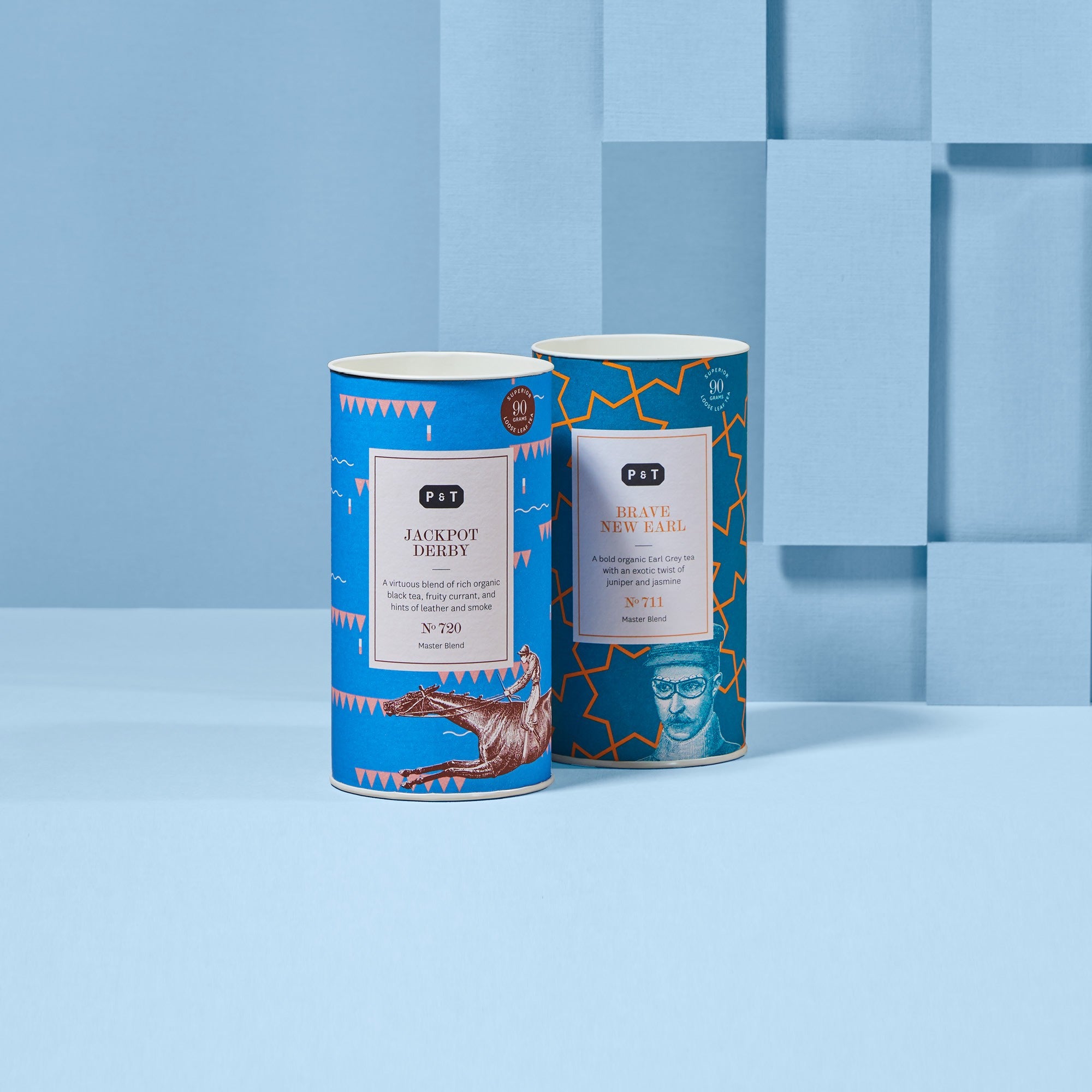 Zwei blaue zylindrische Teedosen mit Premium-Teemischungen vor hellblauem geometrischem Hintergrund