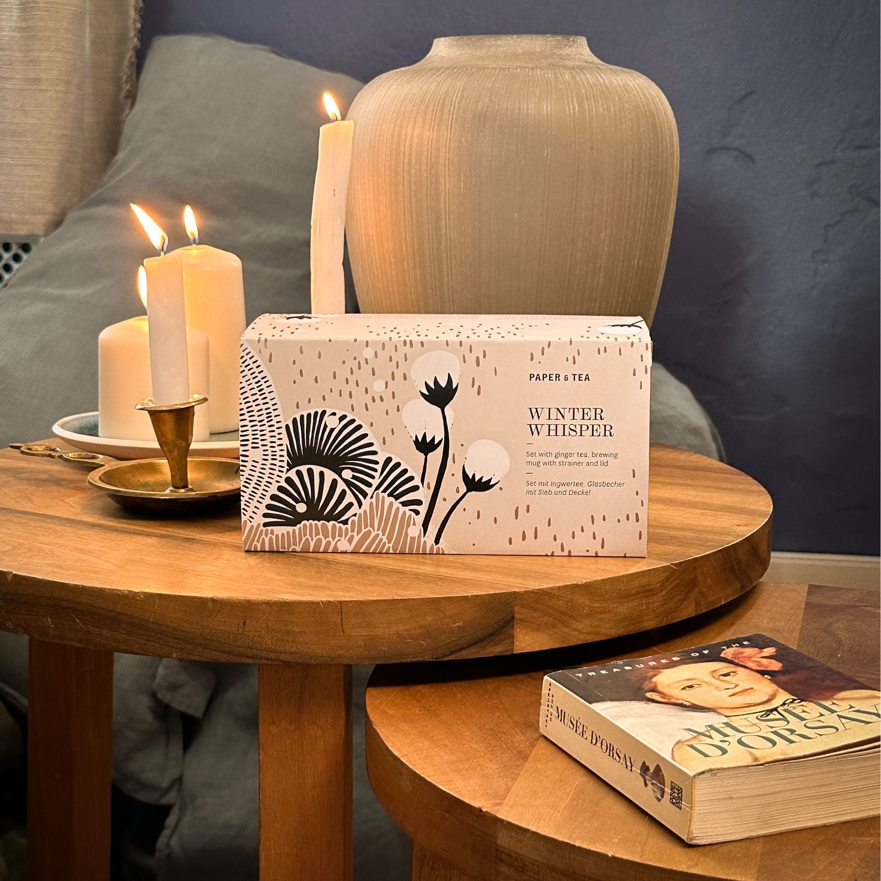 Paper & Tea Winter Whisper Ingwertee-Set auf Holztisch mit Kerzen, Keramikvase und Kunstbuch.