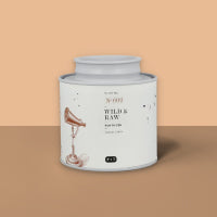 Weißer Körperpeeling-Behälter WILD & RAW mit Vogel-Illustration vor zweifarbigem Hintergrund.