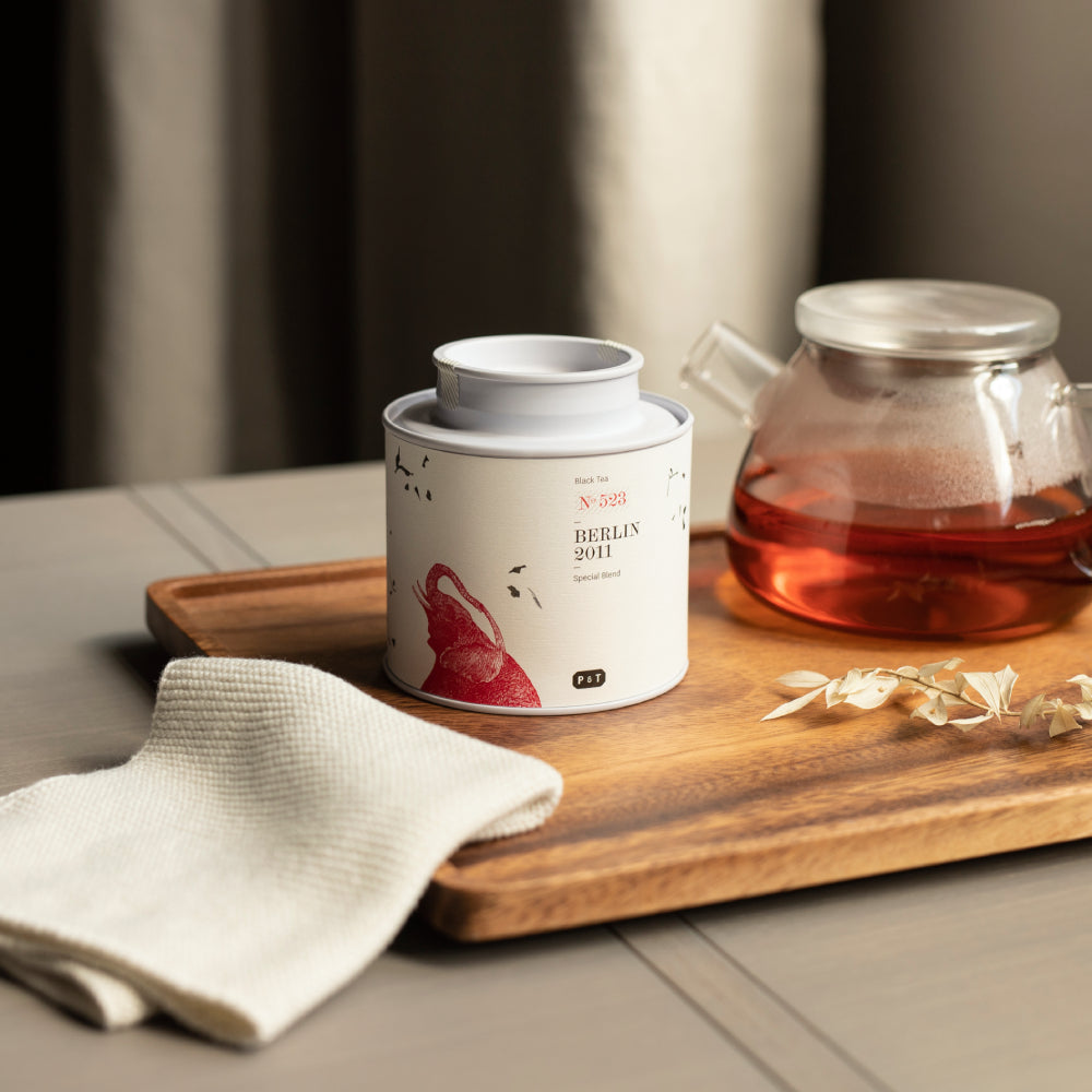 Weiße Teedose mit rotem Elefantenmotiv, Aufschrift ‚Black Tea N-523 Berlin 2011 Special Blend‘, auf Holztablett.