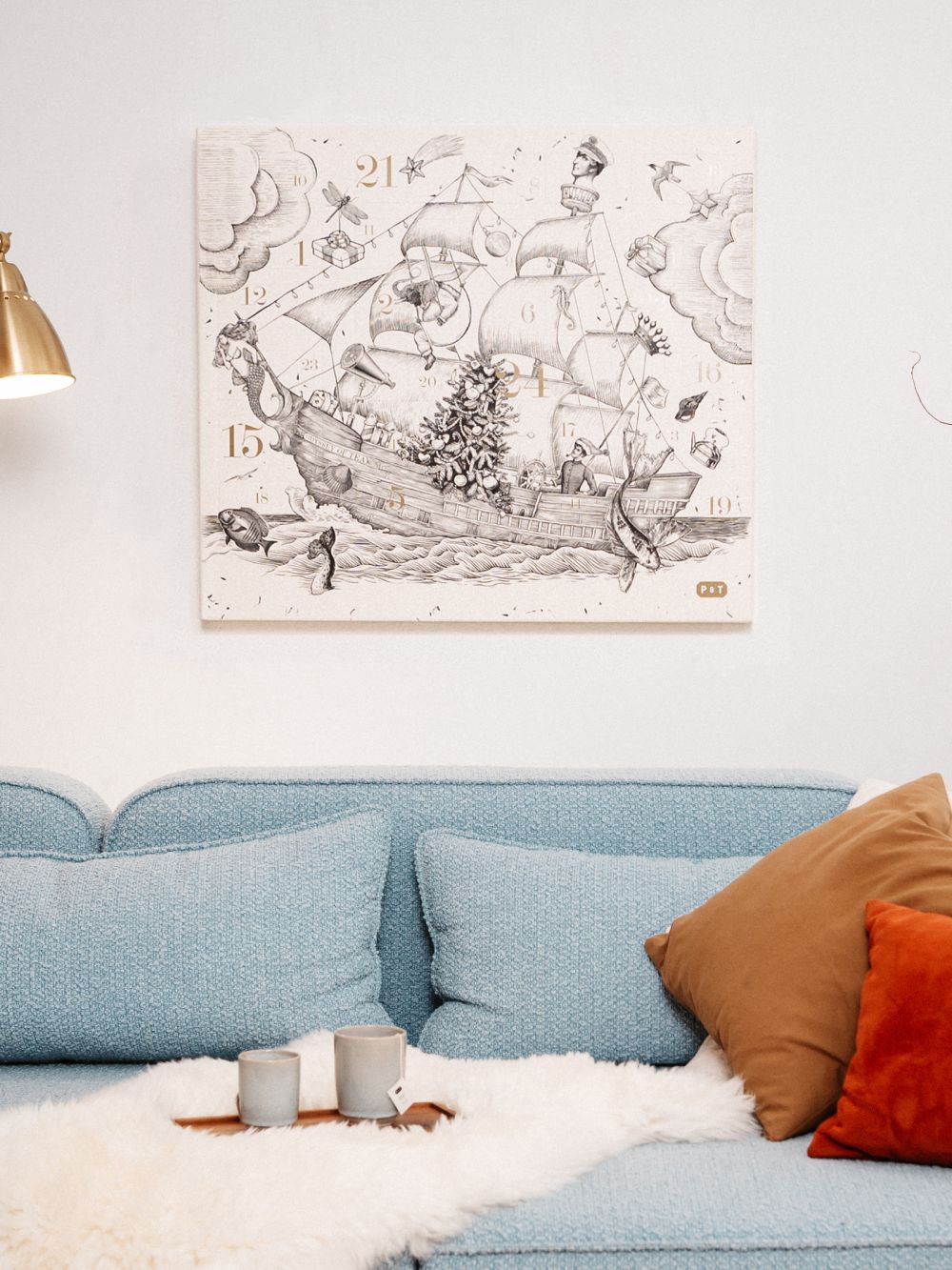 Gemütliche Wohnzimmerecke mit hellblauem Sofa, bunten Kissen und monochromer Schiffskunst mit goldenen Details.