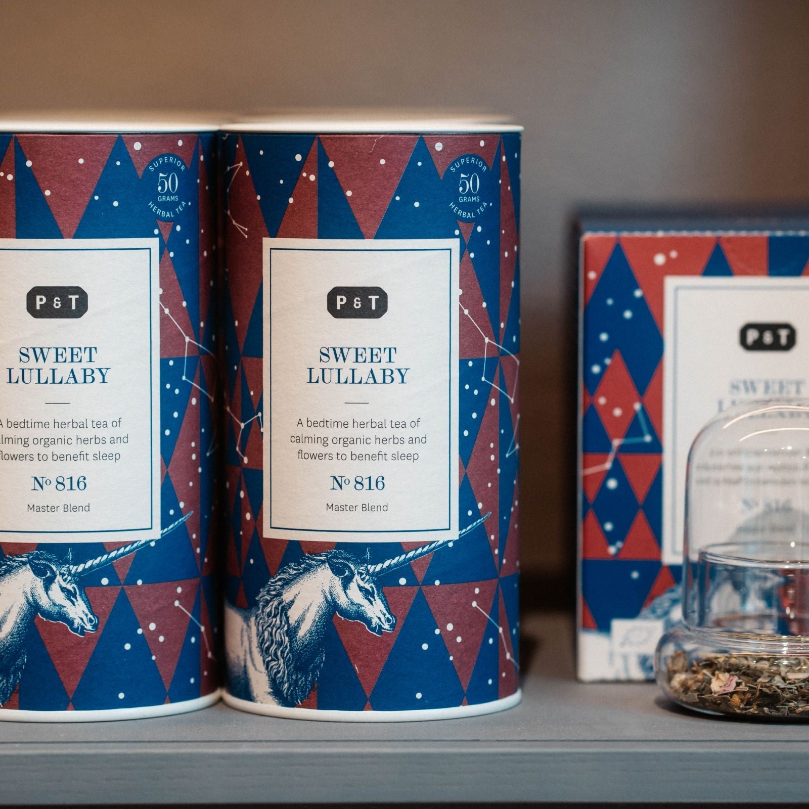 Zwei P & T Süße Wiegenlied Kräutertee-Dosen mit Einhorn-Illustration, lose Teeblätter unter Glaskuppel.