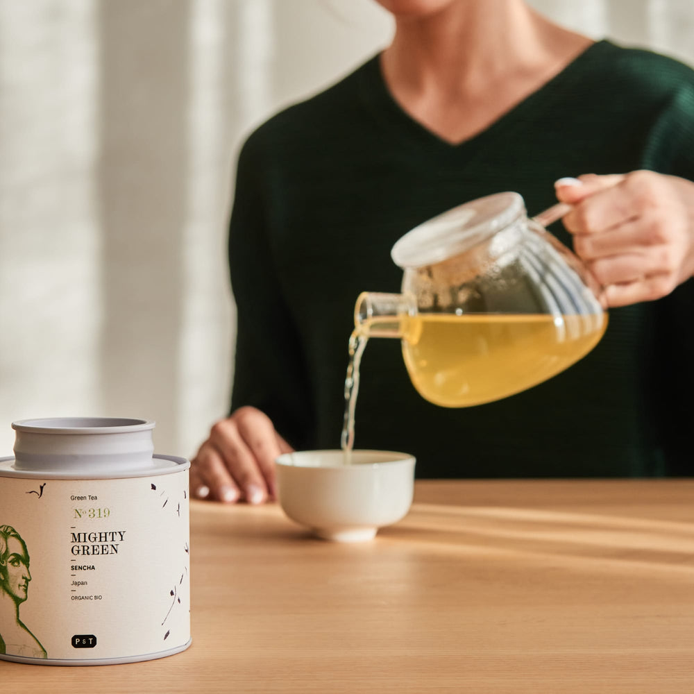Dose mit japanischem Bio-Sencha-Grüntee MIGHTY GREEN und Grüntee in weiße Tasse auf Holztisch