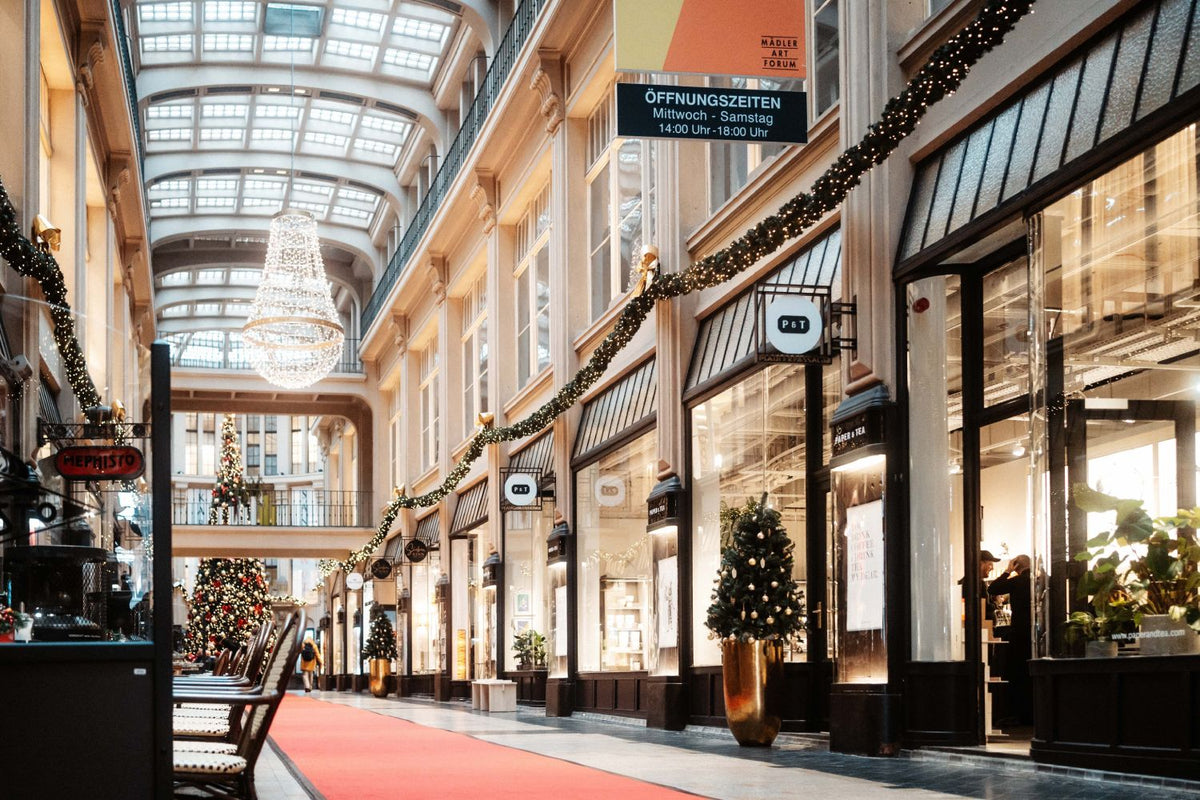 Festlich geschmückte Einkaufspassage mit Glasdach, Kronleuchter, Weihnachtsbäumen und P&T Teegeschäft.