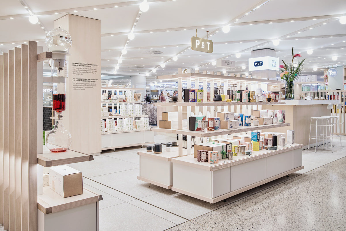Moderner P & T Teeladen mit Holzregalen, bunten Teeschachteln und Barbereich mit Hockern.