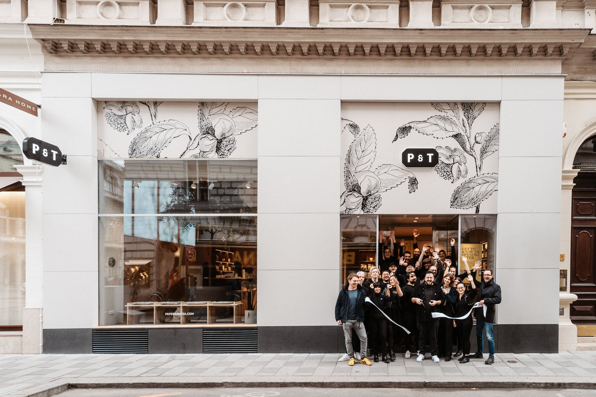 Fröhliche Gruppe vor P&T Teeladen mit weißer Fassade und botanischen Illustrationen.