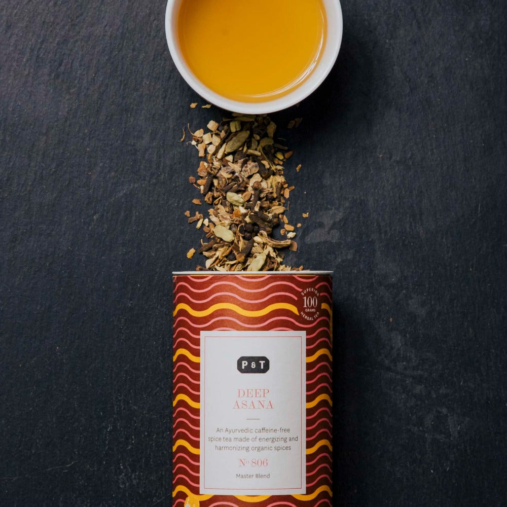 Geöffnete Teedose 'P & T DEEP ASANA' mit Wellenmuster, losem Gewürztee und Tasse gelb-orangem Tee.