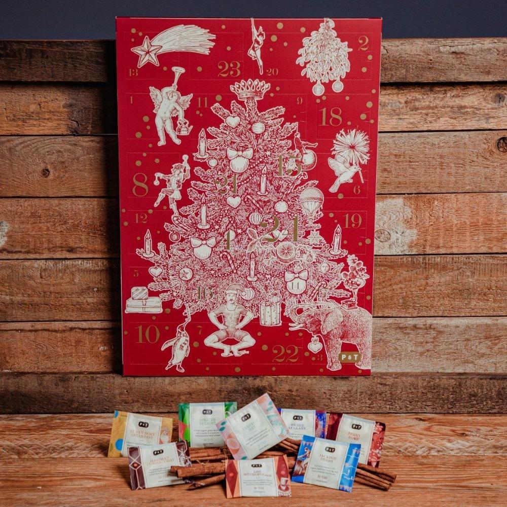 Roter Adventskalender mit weißem Weihnachtsbaum und Pralinen auf Zimtstangen vor Holzhintergrund.