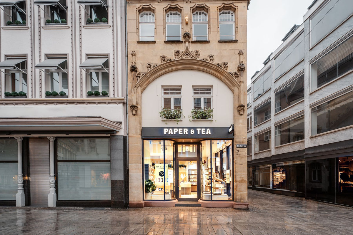 PAPER & TEA Geschäft mit beleuchtetem Eingang und Schaufenster, das eine 10 € Geschenkaktion bewirbt, Mittel-Str.