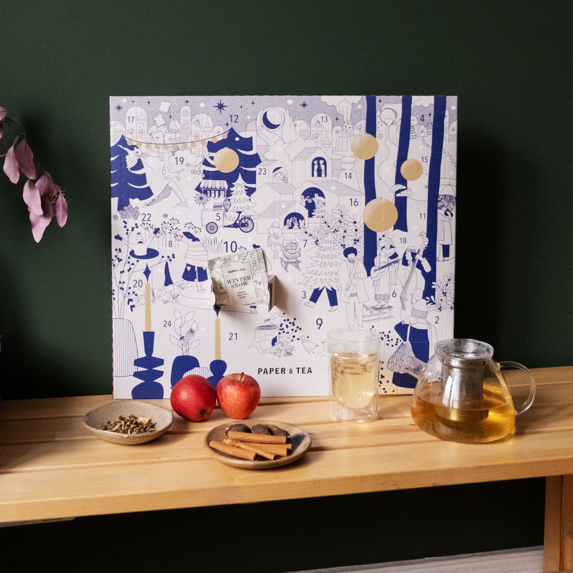 Adventskalender von PAPER & TEA mit blauen, weißen Illustrationen, Glas-Teekanne, Tasse, Äpfeln und Zimt.